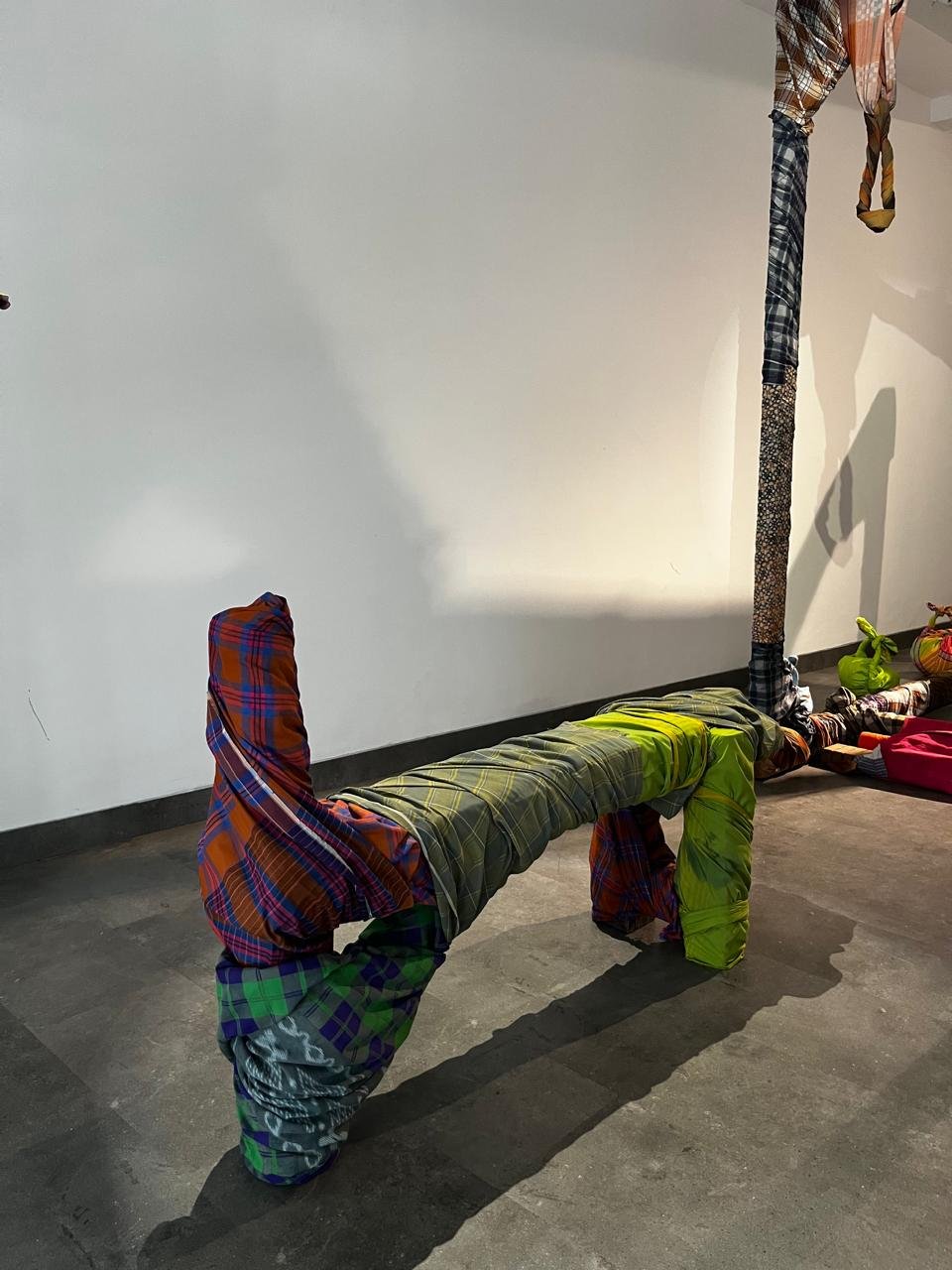 A trestle-like form built from bound sarongs in orange, green and blue plaid