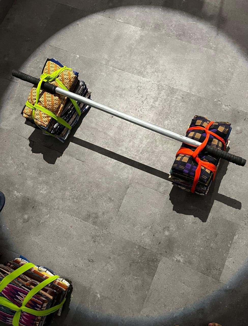 A barbell resting on stacks of folded sarongs, seen from above in a pool of light